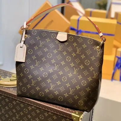 A brown monogram-canvas tote bag with tan leather handles standing on a wooden desk