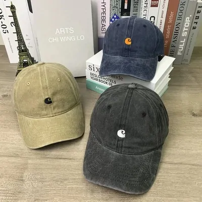 Three washed cotton baseball caps in olive, black and charcoal resting against a stack of books