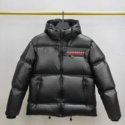 A black quilted hooded puffer jacket hanging in front of a yellow backdrop