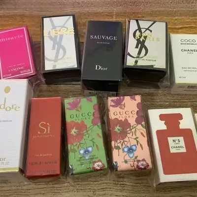Ten boxed designer fragrances laid out on a wooden surface, including Dior Sauvage, Chanel No 5 and two floral Gucci boxes